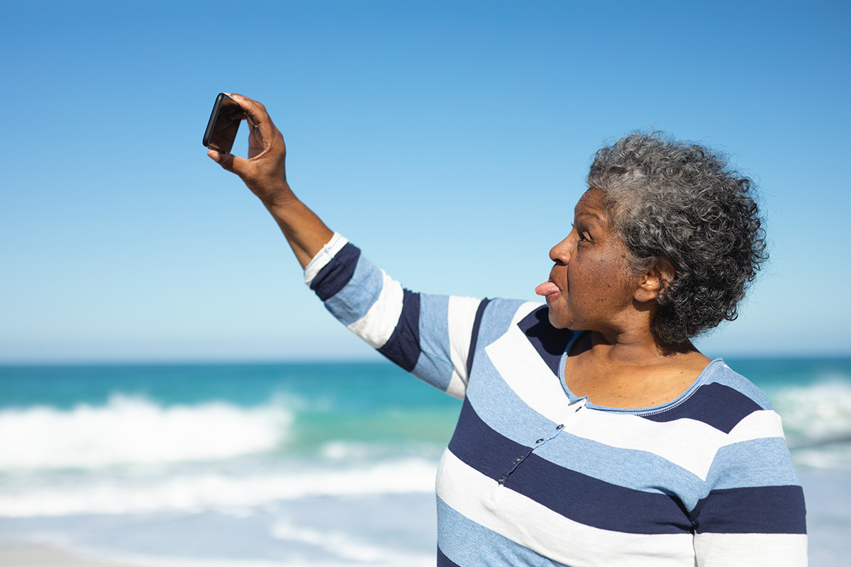 An older black woman taking selfies at the beach